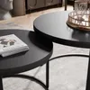A close-up view of two round coffee tables, one nested slightly under the other, on a textured rug. A magazine is placed on the smaller table. Voir les images du produit