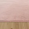 A close-up view of a pink shaggy rug on a wooden floor. Voir les images du produit