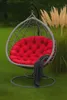 A hanging egg chair with a red cushion and a dark gray blanket is placed on a green lawn next to tall, tan ornamental grasses. Produktbild-Vorschau