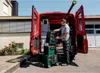 A man is loading toolboxes into the back of a red van. Produktbild-Vorschau
