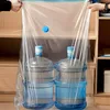 Two large water bottles are placed inside a clear vacuum storage bag, which is being held open by two hands. The background shows shelves of a closet or storage unit. Voir les images du produit