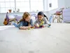 Two young girls are playing with LEGOs on the floor in a bright room. Produktbild-Vorschau