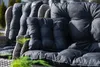 Close-up of outdoor chair cushions on a wicker chair frame, with greenery in the foreground. Produktbild-Vorschau