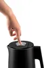 A hand is pressing the button on top of a black electric kettle. Podgląd zdjęcia produktu
