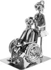A metal figurine of a caregiver assisting a person in a wheelchair, made from nuts, bolts, and other hardware. Voir les images du produit