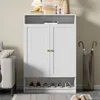 A white shoe cabinet with gold handles is shown in a room next to a sofa and an umbrella stand. Produktbild-Vorschau