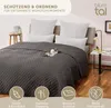A bed with a dark gray quilted bedspread and pillows, with a cat lying on the bedspread. There are decorative icons at the bottom of the image. Náhled obrázku produktu