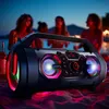 A portable Bluetooth speaker is set up on a beach at dusk, with people in the background enjoying themselves. Produktbild-Vorschau