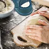 Hands kneading dough on a wooden board, with a bowl of flour and a dumpling maker in the background. Podgląd zdjęcia produktu