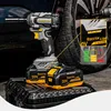 A cordless impact wrench with two batteries is displayed on a black textured surface, with a car tire and wheel in the background. A magnified inset shows battery charge indicators and product details. Produktbild-Vorschau
