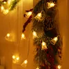 A close-up shot of a Christmas garland with bell-shaped lights, pine cones, and red berries. Náhled obrázku produktu