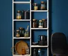 A white shelving unit filled with various storage jars and a woven tray against a dark blue wall. Produktbild-Vorschau