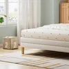 A close-up view of a bed with patterned sheets, placed on a rug in a room with a window and a storage cube. Produktbild-Vorschau