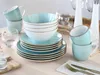 A set of aqua-colored ceramic dishes, including bowls and cups, are neatly stacked on a light-colored wooden table. Produktbild-Vorschau