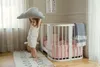 A young child is playing with a cloud pillow next to a crib in a nursery. Produktbild-Vorschau