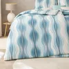 A close-up view of a bed with blue and white wavy patterned bedding. Produktbild-Vorschau