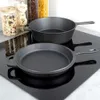 Two cast iron pans are placed on a black induction hob, with jars of food items in the background. Náhled obrázku produktu
