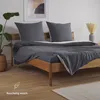 A bed with grey bedding and pillows in a room with a plant and artwork. Voir les images du produit