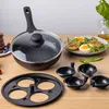 A frying pan with a lid, an egg insert, and a plate of food are arranged on a wooden table. Voir les images du produit