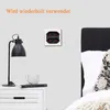 A bedside table with a lamp, a book, and a mug, next to a wall with an electrical outlet and a bed. Produktbild-Vorschau