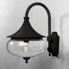 A black outdoor wall light with a clear glass shade is mounted on a light gray wall. Produktbild-Vorschau