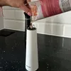 A hand is pouring contents from a package into a white spice grinder, with a black spice grinder in the background. Produktbild-Vorschau