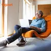 A man sits in an orange chair using a laptop. Náhled obrázku produktu