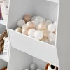 A close-up view of a white shelf filled with colorful balls and a stuffed toy. Produktbild-Vorschau