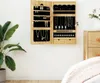 A wooden jewelry cabinet with a mirror is mounted on a white wall next to a large potted plant and a dresser. A bed is partially visible in the foreground. Produktbild-Vorschau