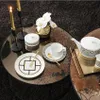 A tea set and plates are arranged on a coffee table with candles and flowers. Voir les images du produit