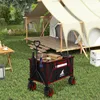 A camping scene with a tent, a table, and a wagon filled with camping supplies. Produktbild-Vorschau
