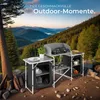A camping kitchen setup in a natural outdoor environment with mountains and trees in the background. Produktbild-Vorschau