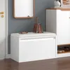 A white storage bench with a cushioned top is shown in an entryway, next to a door and a cabinet. A handbag and gloves are placed on top of the bench. Shoes are visible on a shelf below the cabinet. Produktbild-Vorschau