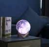 A galaxy-themed moon lamp sits on a nightstand next to two books, with a dark blue couch in the background. Náhľad obrázku produktu