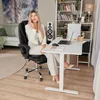 A woman is sitting at a standing desk in a home office setting, talking on the phone. Produktbild-Vorschau