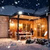 People gathered around a table on a patio in the snow at night, illuminated by outdoor lights. Produktbild-Vorschau