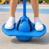 Füße eines Kindes auf einem blauen Pogo-Ball, der dessen Verwendung im Freien auf einer gepflasterten Fläche zeigt Podgląd zdjęcia produktu