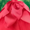 A close-up of a doll's red dress with petal-like layers, set against a blurred green background with sparkling lights. Anteprima dell’immagine prodotto