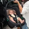 A woman is holding a baby in a car seat next to an open car door. Náhľad obrázku produktu