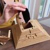A person's hands are shown assembling a wooden pyramid puzzle, holding a small black pouch over the opening. Podgląd zdjęcia produktu