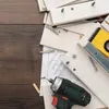 A collection of wooden planks and tools for furniture assembly, including a drill, level, and screws, laid out on a wooden surface. Produktbild-Vorschau