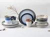 A collection of stoneware dishes and mugs arranged on a white surface with a dried plant sprig. Náhľad obrázku produktu