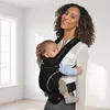 A woman is holding a baby in a black baby carrier. Produktbild-Vorschau