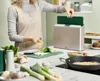 A person is preparing food in a kitchen, with a set of cutting boards in the background. Anteprima dell’immagine prodotto