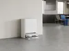 A white robot vacuum cleaner with its charging dock is positioned against a white wall in a modern, minimalist room. Náhled obrázku produktu