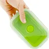 A hand holding a green silicone food container filled with a green liquid. Produktbild-Vorschau