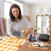 A woman is sewing on a table with various sewing supplies. Produktbild-Vorschau