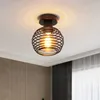 A black metal cage ceiling light fixture with a visible bulb is mounted on a white ceiling. Produktbild-Vorschau