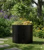 A black compost bin filled with garden waste sits on a grassy lawn surrounded by flowers and trees. Produktbild-Vorschau