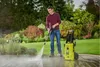 A man is pressure washing a wooden deck in a garden setting. Produktbild-Vorschau